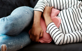 Cropped shot of a woman holding a hot water bottle against her stomach on the sofa at home.